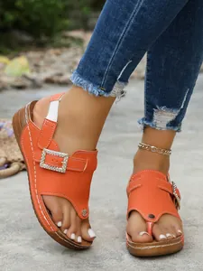 Close-up of orange wedge thong sandals with rhinestone buckle and elastic strap