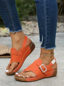 Close-up detail shot of vibrant orange wedge sandals featuring a sparkling rhinestone buckle.