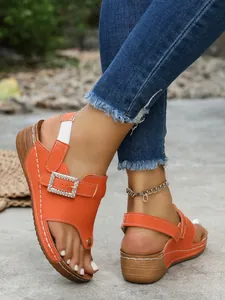 Close-up of vibrant orange wedge sandals with rhinestone square buckle and toe ring.