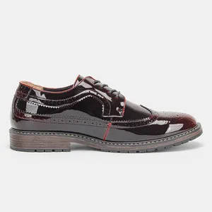 Detalle lateral de zapatos Brogue para hombre en charol burdeos con costuras rojas.