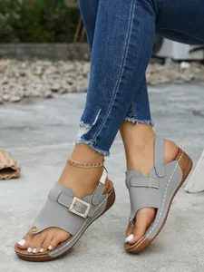 Stylish grey wedge thong sandals with decorative rhinestone buckle shown with denim jeans