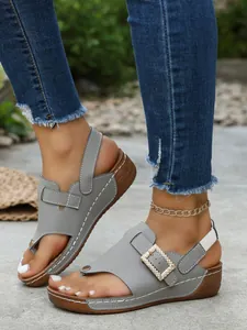 Close-up of stylish grey wedge sandals featuring a sparkling rhinestone buckle and clip-toe design