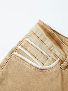 Macro detail of men's mustard yellow stretch jeans featuring white decorative piping on pockets