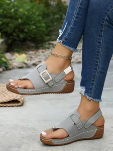 Close-up view of grey wedge sandals with rhinestone square buckle and toe-post design.