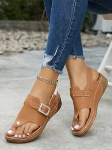 Detailed view of brown thong wedge sandals featuring a rhinestone buckle and white stitching.