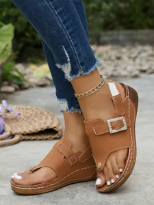 Detailed view of brown wedge sandals with rhinestone buckle on a model outdoors.
