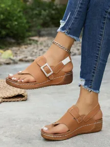 Detailed view of women's tan wedge sandals featuring a sparkling rhinestone buckle