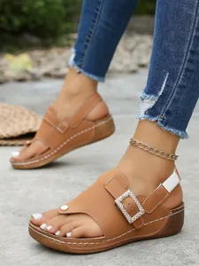 Fashionable brown wedge thong sandals featuring a sparkling rhinestone buckle detail.