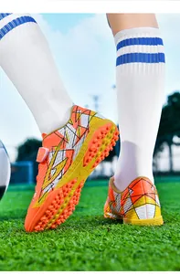 Detail van kunstgras voetbalschoenen voor kinderen met oranje patroon en TF-rubberzool.