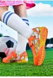 Detailweergave van oranje kindervoetbalschoenen met klittenband op een grasveld