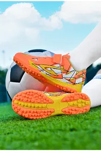 Detailopname van oranje kindervoetbalschoenen met TF-rubberen zool en klittenbandsluiting.