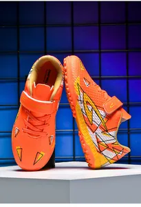 Detailopname van oranje kindervoetbalschoenen met klittenbandsluiting en rubberen TF-zool