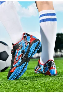 Detailweergave van kindervoetbalschoenen met TF-rubberen zool op groen grasveld.