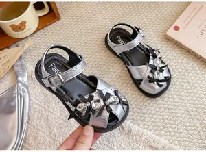 Nahaufnahme der silbernen Mädchensandalen mit Strass und schwarzen Schleifen