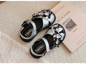 Nahaufnahme silberner Mädchensandalen mit funkelnden Strassschleifen auf einem Buch