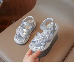 Close-up of silver girl's sandals with elegant bow, pearl, and rhinestone details.