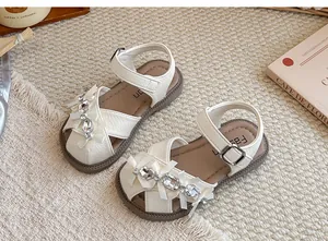 Nahaufnahme weißer Mädchen-Sandalen mit eleganten Strass-Schleifen und weichen Sohlen