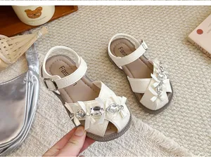 Detailansicht von cremefarbenen Mädchen-Sandalen mit Strasssteinen und Schleifen