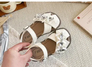 Detailansicht weißer Mädchensandalen mit glitzernden Strasssteinen und Schleifen.
