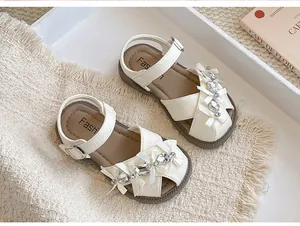 Detailansicht weißer Mädchensandalen mit glitzernden Strasssteinen und Schleifen.