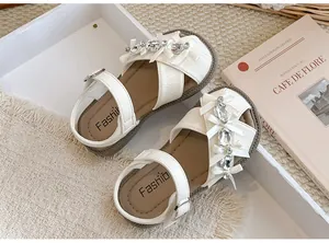 Detailansicht weißer Mädchensandalen mit glitzernden Strasssteinen und feinen Schleifen