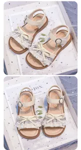 Detailed view of cream girls' sandals with delicate lace trim and bowknot detail.
