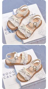 Close-up of cream girls' sandals featuring elegant lace bow and soft sole detail