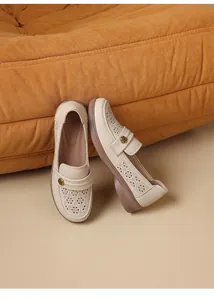 Detail view of beige hollow-out loafers leaning against an orange textured sofa
