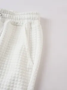 Close-up detail of white men's fashion sports shorts featuring quilted grid texture and elastic waist