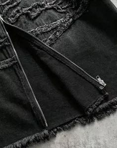 Gros plan détaillé sur une chemise en denim noir avec franges et fermeture éclair.
