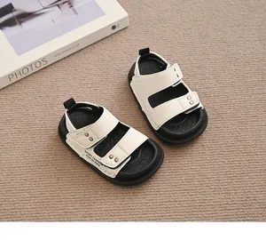 Cremeweiße Kindersandalen mit schwarzen Sohlen und Klettverschluss auf Beige.