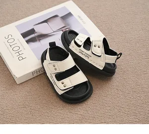 Modische cremefarbene und schwarze Kinder-Sommersandalen auf einem Fashion-Buch-Hintergrund.