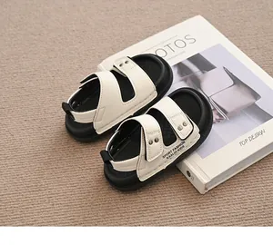 Nahaufnahme von stilvollen cremefarbenen und schwarzen Kindersandalen auf weißem Buch