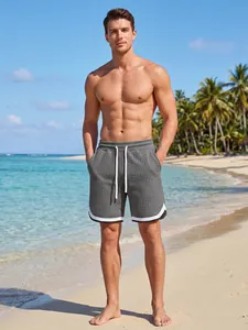 Detailed view of men's grey checkered swim shorts on a tropical beach setting