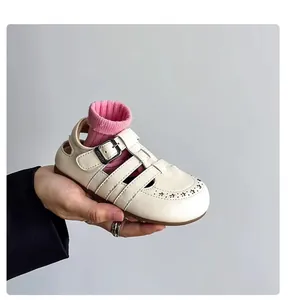Close-up of cream vintage hollow-out leather sandal for children with soft sole.