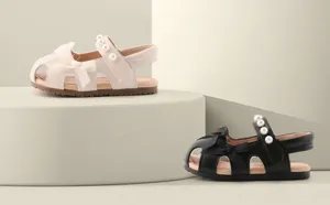 Détail de sandales pour bébés filles avec nœuds et perles sur plateforme épurée