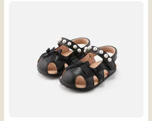 Nahaufnahme schwarzer Babysandalen für Mädchen mit Schleifen und Perlenverzierung.