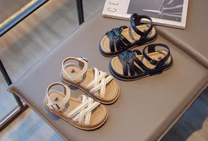 Gros plan de sandales romaines pour filles avec brides croisées en noir et beige.