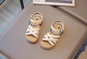 Détail de sandales romaines pour filles avec brides beiges croisées et logo cœur.