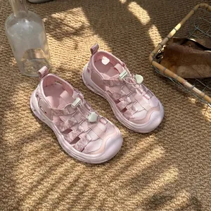 Pink kids closed-toe sandals with breathable mesh and drawstring on a woven rug