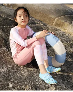 Ein Mädchen sitzt auf Felsen und trägt blaue Wasserschuhe mit Cartoon-Muster am Strand
