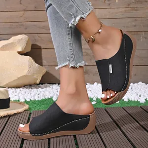 Detail of black laser-cut wedge sandals on model foot with outdoor summer scenery
