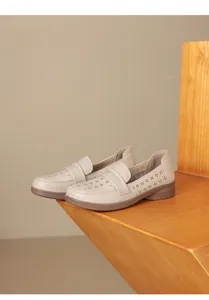Detailed view of comfortable beige hollow-out leather loafers on a minimalist wooden stand.