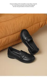 Close-up detail of black soft leather loafers with hollow-out pattern on beige floor.