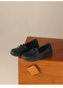 Detailansicht der schwarzen Weichlederslipper mit eleganten Hohlmustern und dekorativer Schleife
