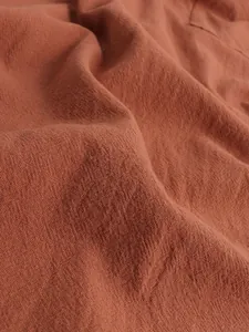 Close-up of terracotta linen fabric texture showing the breathable weave of the men's robe