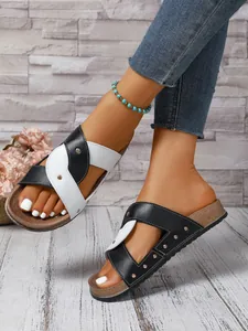 Detail view of stylish women's cross-strap sandals with rivets on a cork-style sole.
