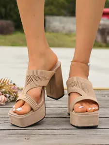 Dettaglio di sabot con zeppa in maglia beige e tacco largo su un pavimento in legno