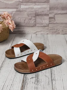 Detailed view of women's cross-strap sandals with gold rivet accents on wooden floor
