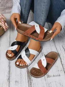 Close-up of stylish cross-strap slides with rivets in black and brown colors